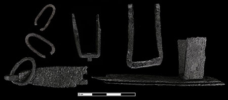 A closeup image of a ski-shaped rough lock with a carriage wheel sitting on it. The ski is hooked to a heavy iron chain that extends beyond the bounds of the photo.